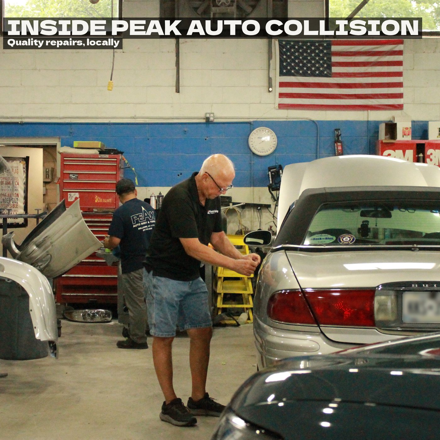 Inside the Peak Auto Collision shop: one man detailing a silver convertible while a technician works on panels behind him, under an American flag