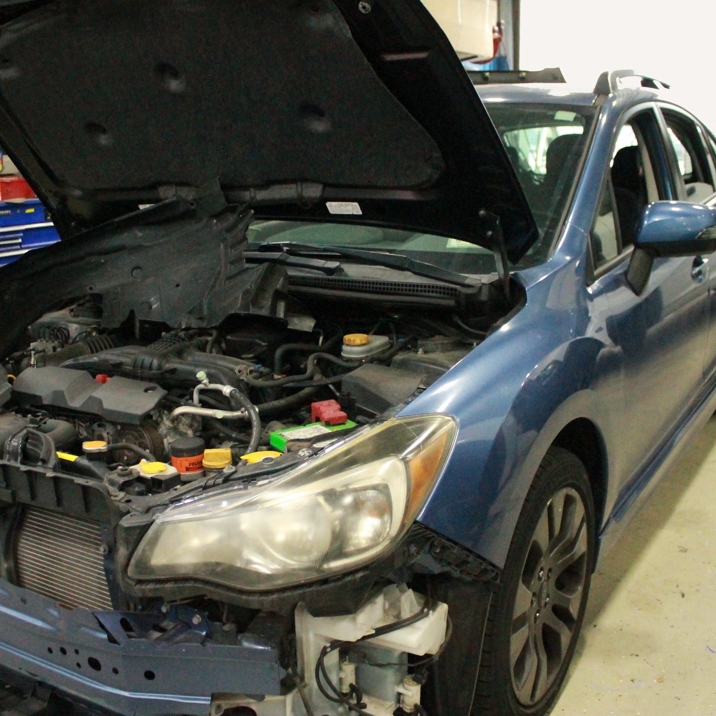 Blue Subaru with the hood up and front bumper removed during a front end repair
