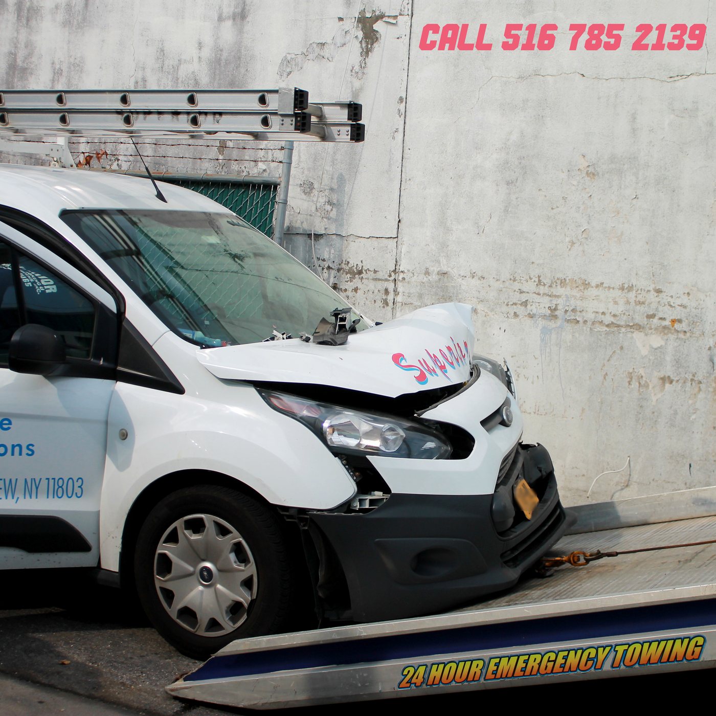 A damaged white work van with a crumpled front end being winched onto a Peak Auto Collision flatbed tow truck